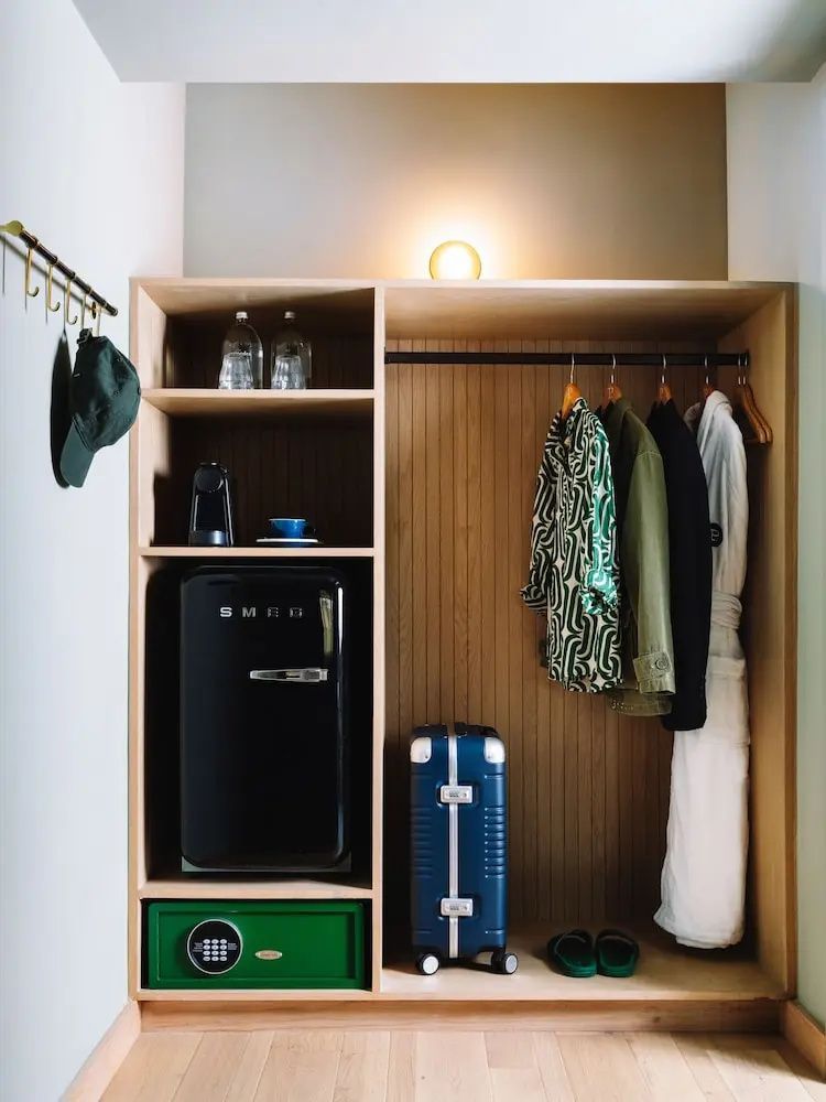 Offener Holzkleiderschrank mit Minikühlschrank, Tresor, Kleidung und Koffer.