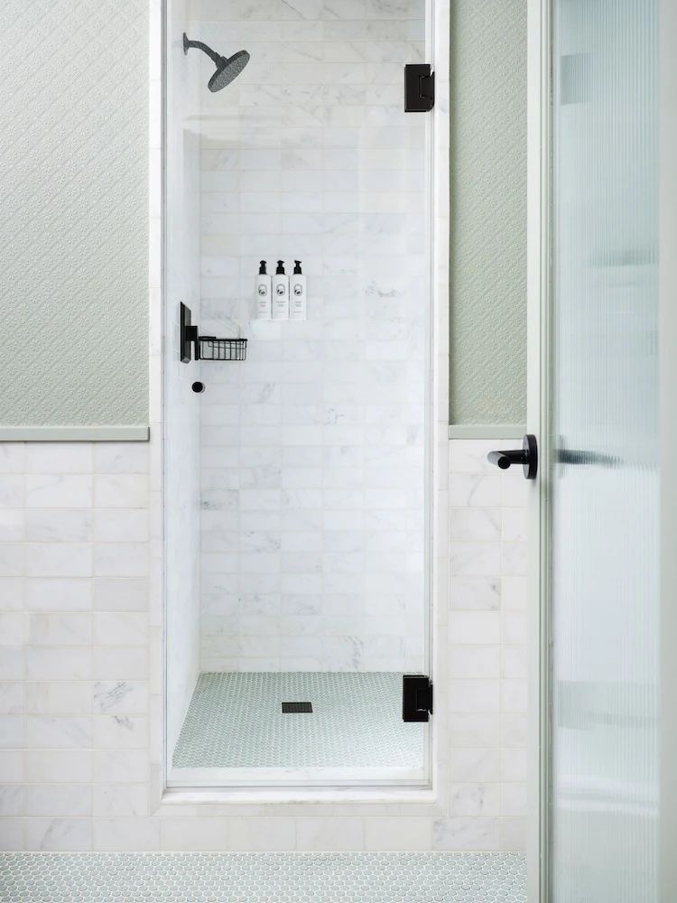 Moderne begehbare Dusche mit hellen Marmorfliesen und Glasabtrennung.