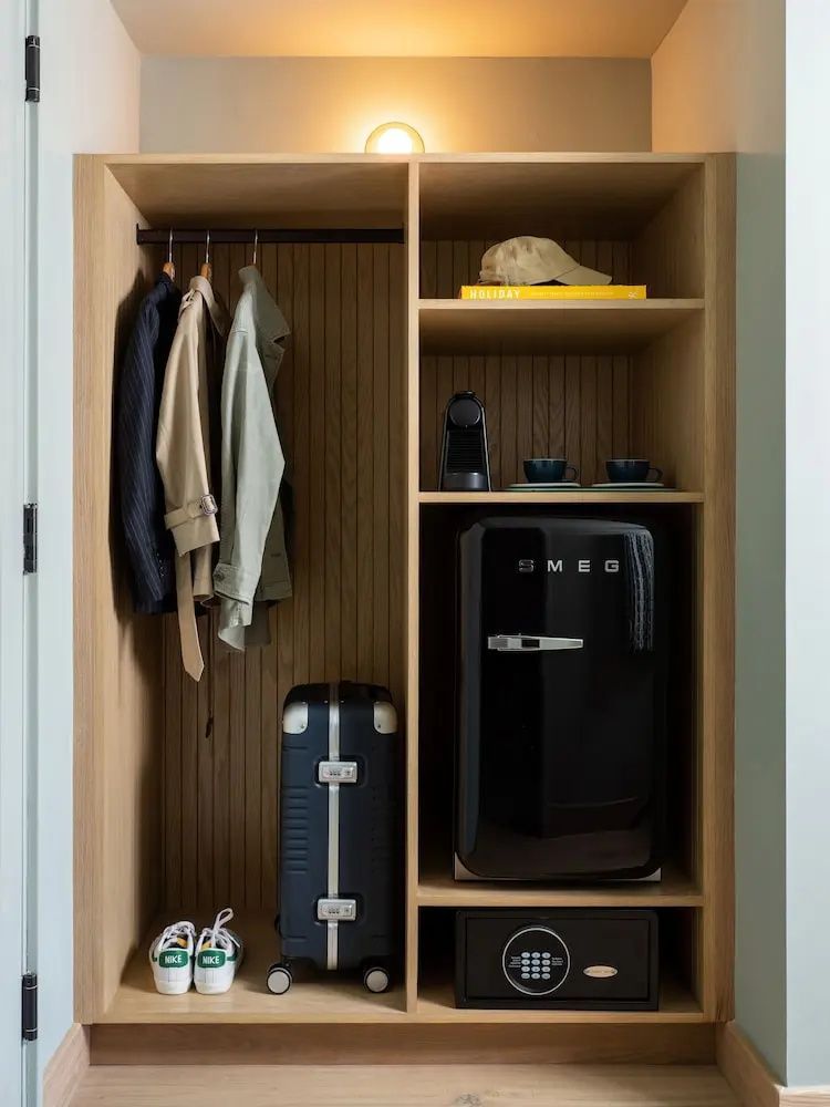 Offener Kleiderschrank aus Holz mit Minibar, Kaffeemaschine, Koffer und Garderobe.