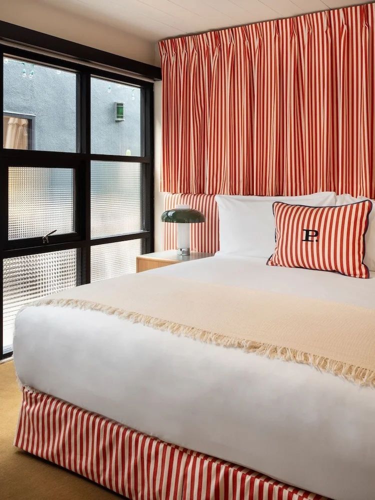 Doppelbett mit rot und weiß gestreiftem Kissen vor einer dunklen Fensterfront.