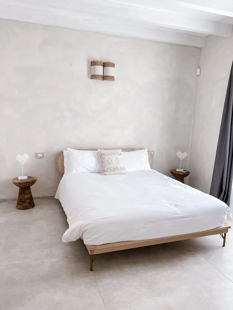 Schlichtes Doppelbett mit weißer Bettwäsche und zwei kleinen Holzbeistelltischen an der Wand.