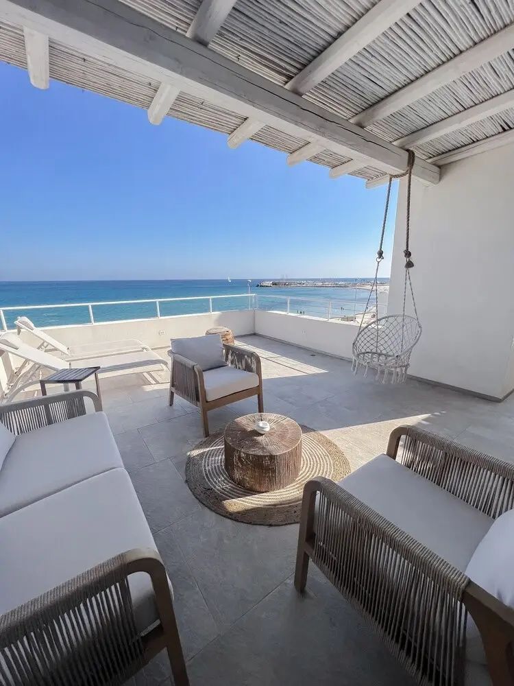 Große Terrasse mit Lounge-Möbeln, Hängesessel und freier Sicht auf das blaue Meer.