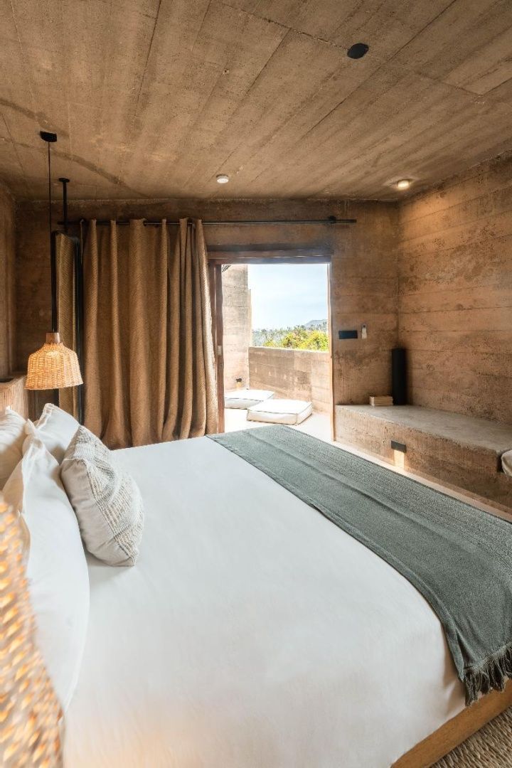 Schlafzimmer mit Doppelbett, Wänden in Stampfbeton-Optik und Blick auf die Terrasse.