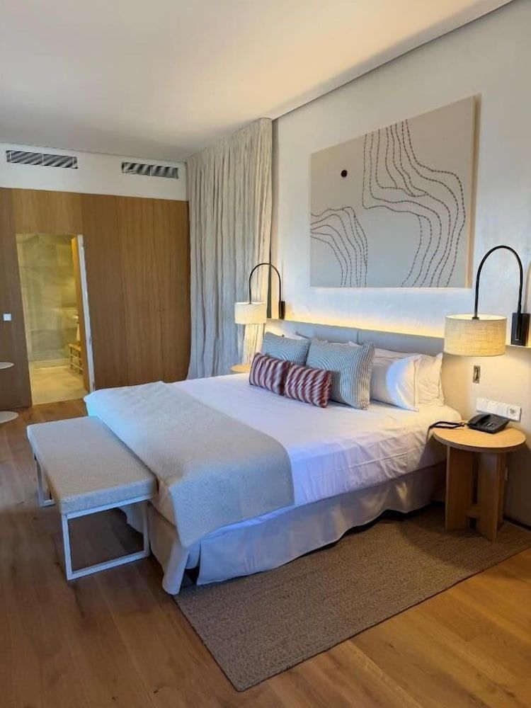 Doppelbett mit hellen Kissen, Holzfußboden und Wandbild in einem modern eingerichteten Hotelzimmer.