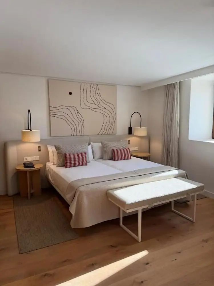 Doppelbett mit hellen Kissen und Wandbild in einem modern eingerichteten Hotelzimmer.