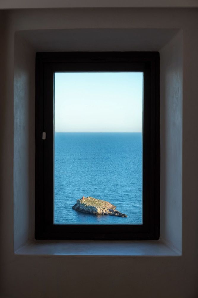 Rahmenfenster mit direkter Sicht auf das ruhige Meer und eine kleine vorgelagerte Felseninsel.