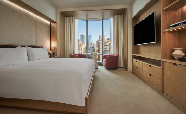 Modernes Hotelzimmer mit Doppelbett, Wand-TV und Sitzecke am Fenster mit Stadtblick.