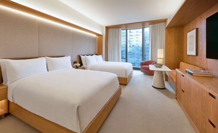 Hotelzimmer mit zwei großen Betten, weißer Bettwäsche, Holzverkleidung und Blick auf die Stadt.