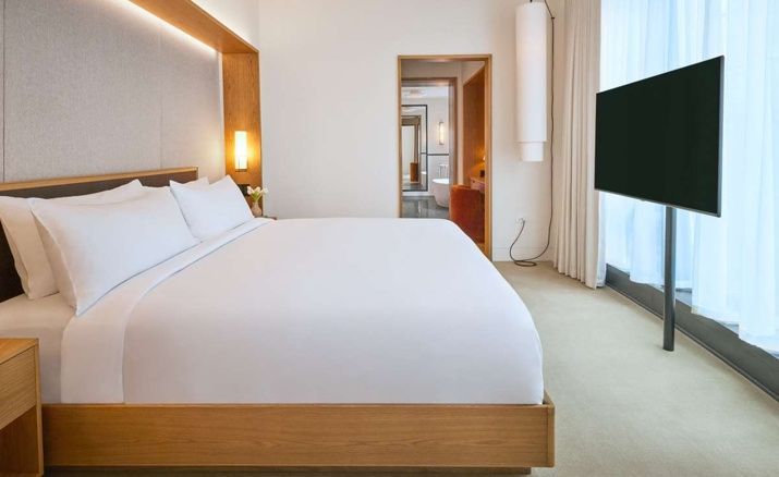 Helles Hotelzimmer mit großem Holzdoppelbett und Durchgang zum Badezimmer.