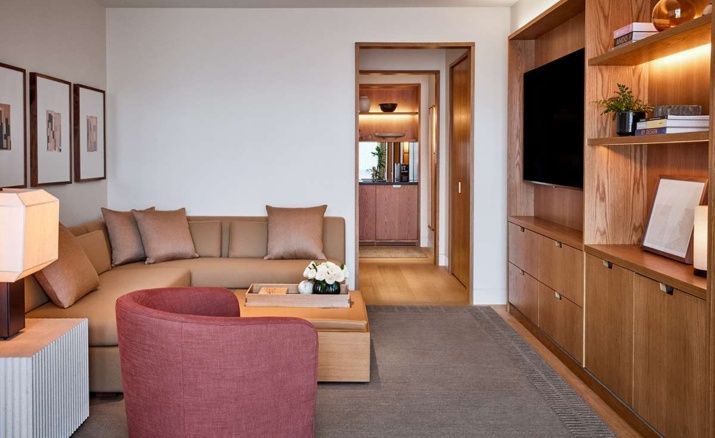 Wohnbereich einer Suite mit braunem Sofa, rotem Sessel und einem Fernseher an der Wand.