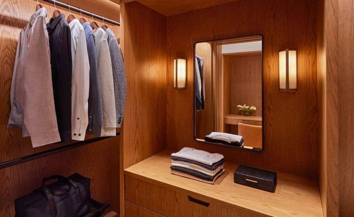 Begehbarer Kleiderschrank aus Holz mit aufgehängter Kleidung, Spiegel und Ablagefläche.