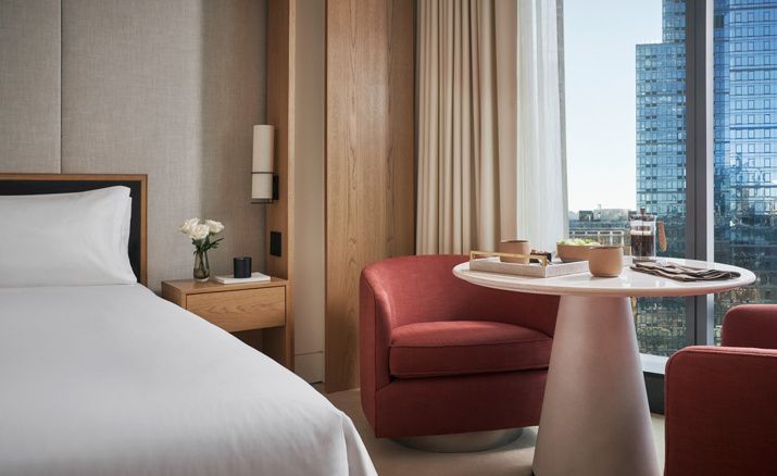 Sitzbereich im Zimmer mit rotem Sessel, Tisch und Nachttisch mit Blumenstrauß.