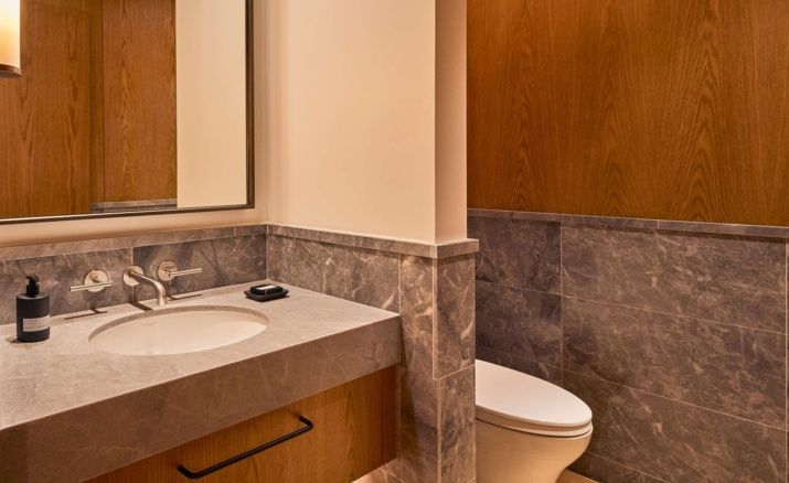 Badezimmer mit Marmorwaschtisch, Spiegel und angrenzender Toilette vor Holzverkleidung.
