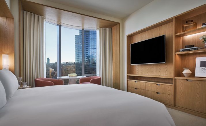 Hell eingerichtetes Hotelzimmer mit Blick auf ein Bett, Fernseher und Panoramafenster.