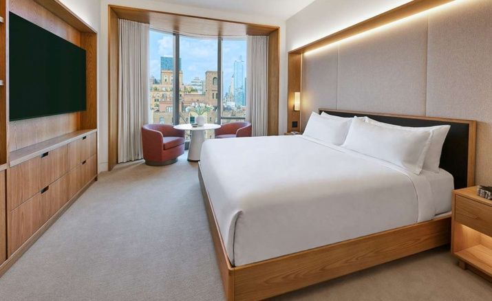 Hotelzimmer mit Holzdoppelbett, hellen Teppichböden und Sitzecke am Fenster.