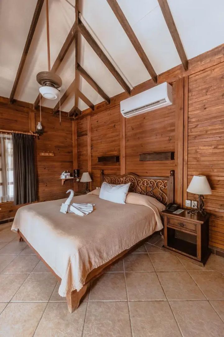 Schlafbereich einer Holzhütte mit großem Doppelbett, Nachttischen und Holzdecke.