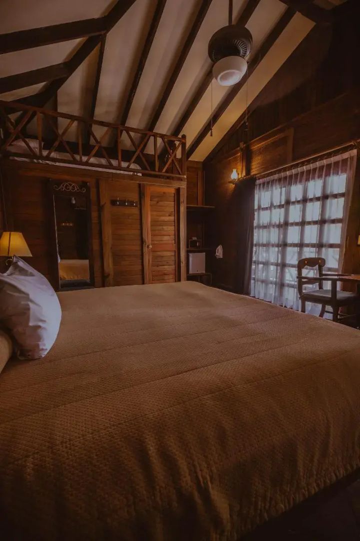 Blick auf das Doppelbett und ein großes Fenster in einem Holzbungalow.