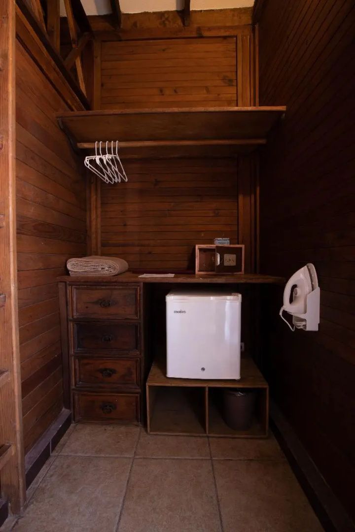 Holzregal mit Minibar, Kommode, Bügelbrett und Bügeleisen im Zimmer.