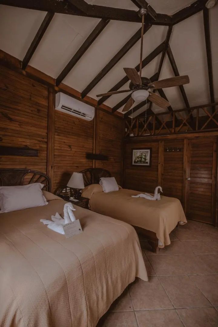 Rustikales Hotelzimmer aus Holz mit zwei Betten, Deckenventilator und Klimaanlage.