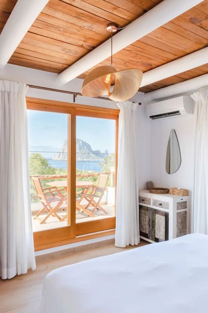 Blick durch die Balkontür auf den Balkon und die Felseninsel Es Vedrà im Meer.