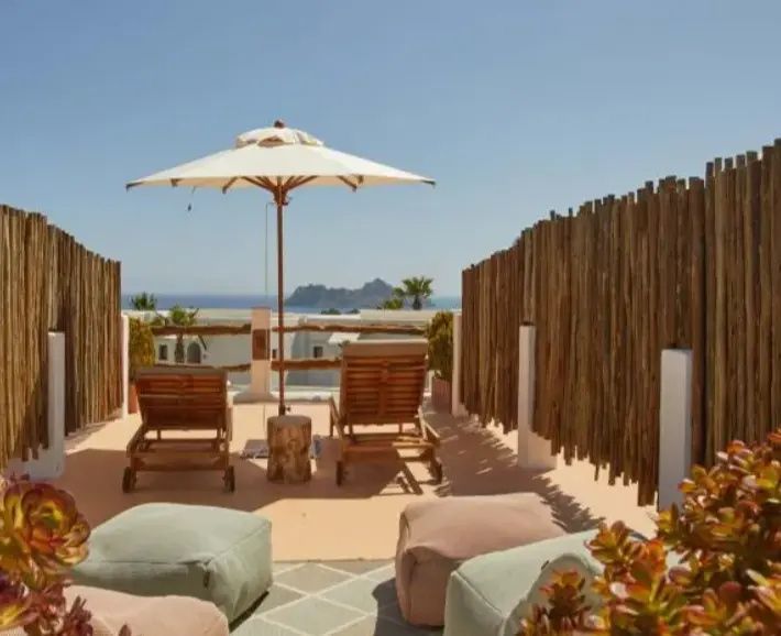 Sonnenterrasse mit zwei Holzliegen, Sonnenschirm und Blick auf das Meer sowie eine Felseninsel.