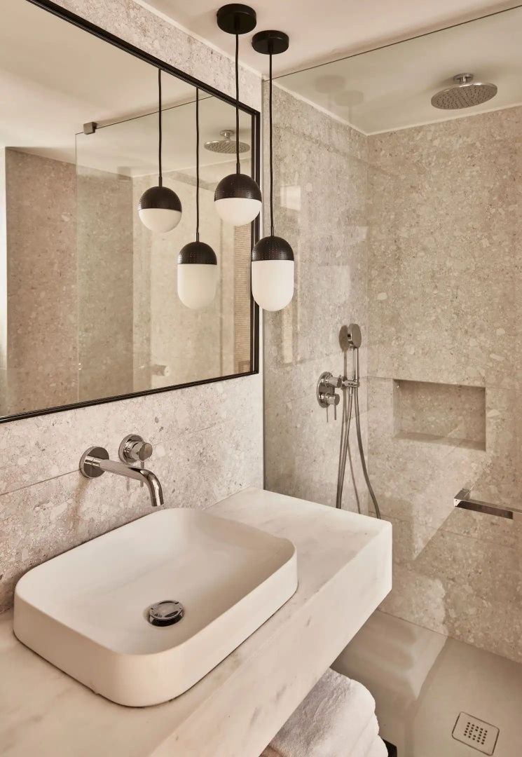 Badezimmer mit hellem Naturstein, modernem Waschbecken und begehbarer Dusche.