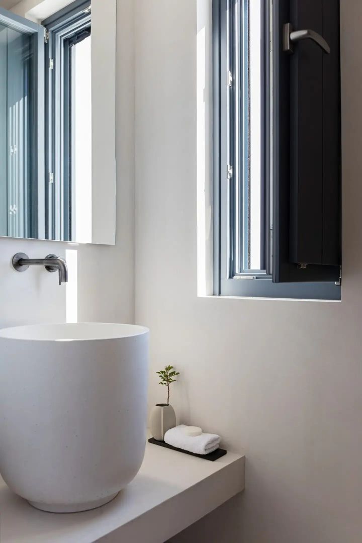 Modernes Badezimmer mit rundem Standwaschbecken, dunkler Armatur und schmalem Fenster.