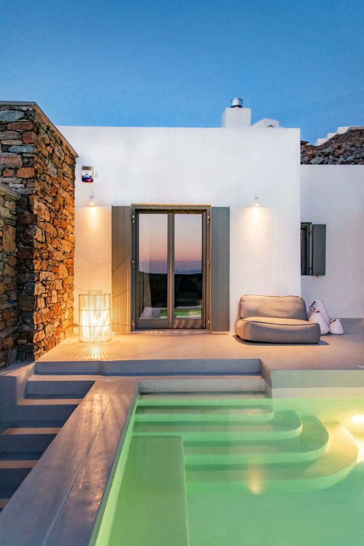 Beleuchteter Pool auf einer Terrasse vor einer weißen Villa bei Dämmerung.