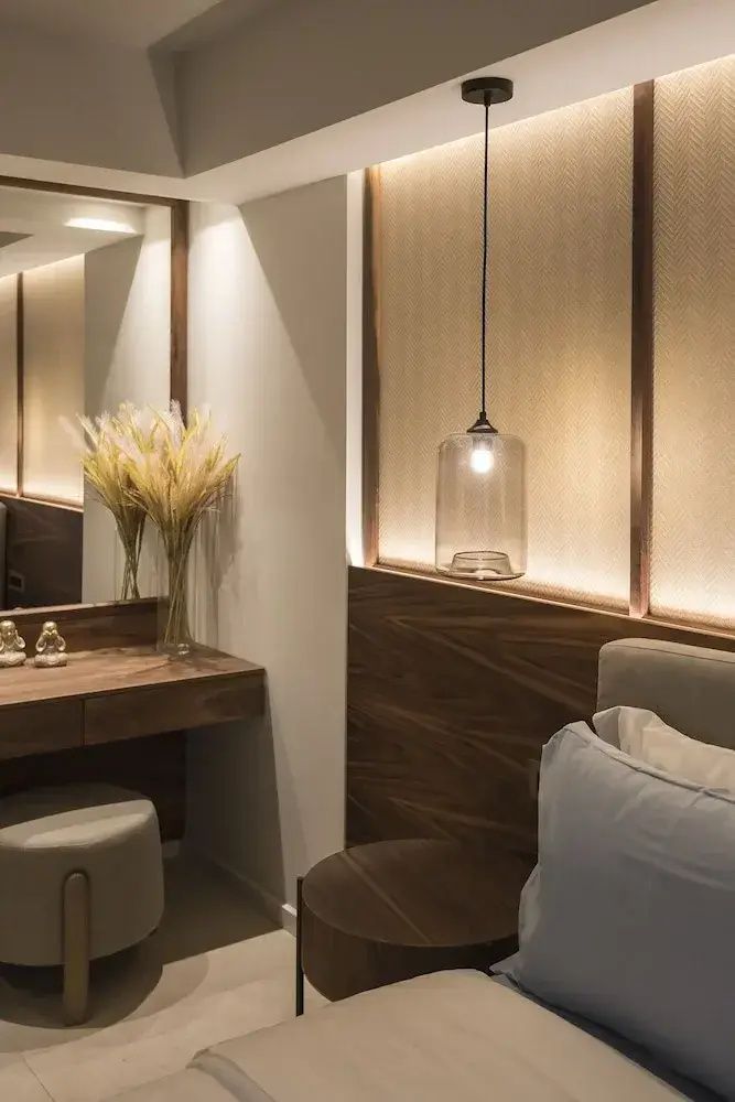 Schminktisch mit Spiegel, Blumenvase und eine hängende Glaslampe neben dem Bett im Hotelzimmer.