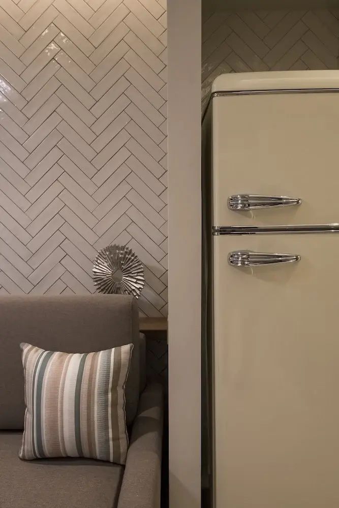 Cremefarbener Kühlschrank neben einer Sitzgelegenheit mit gestreiftem Kissen und Wanddekoration.