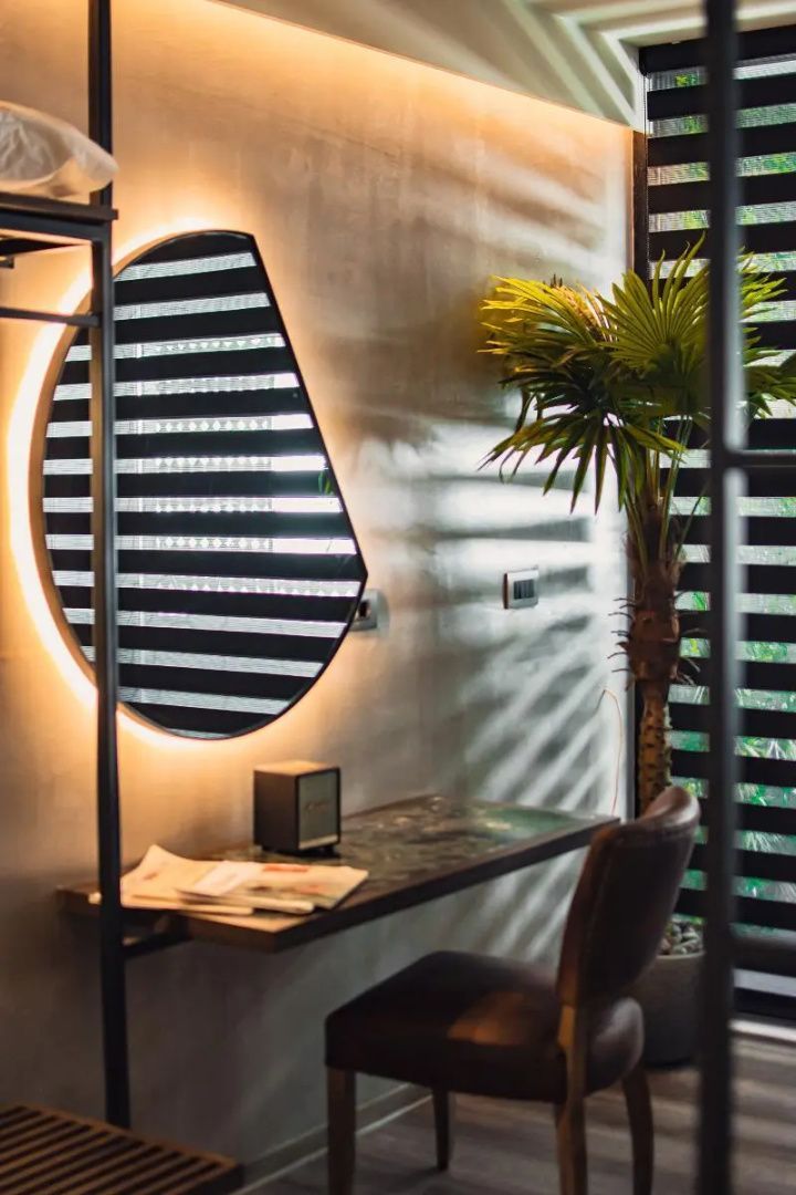 Arbeitsecke im Hotelzimmer mit Schreibtisch, beleuchtetem Spiegel und einer Grünpflanze
