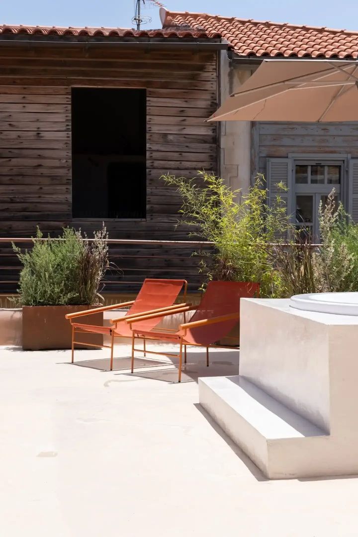 Zwei orangefarbene Liegestühle stehen auf einer Dachterrasse neben Pflanzen.