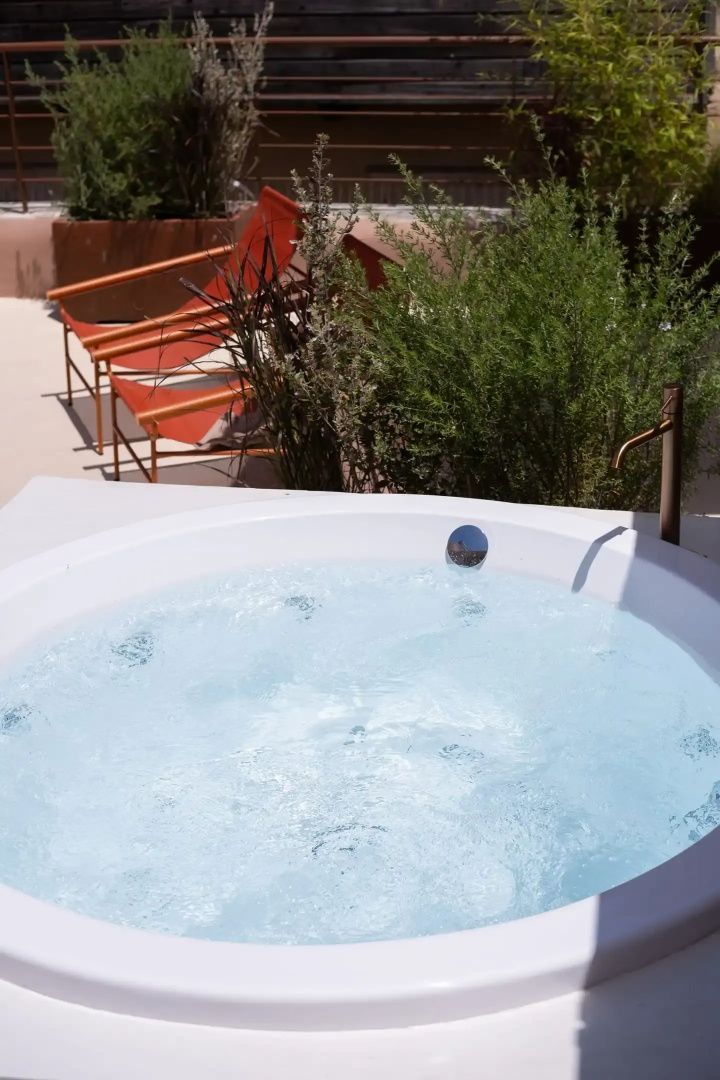 Runder Whirlpool im Außenbereich mit gefülltem Wasser und zwei orangefarbenen Liegestühlen.