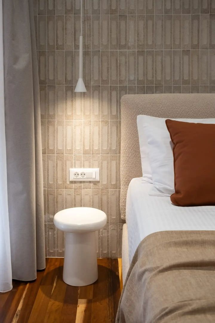 Bett mit braunem Kissen, gepolstertem Kopfteil und einem kleinen weißen Beistelltisch.