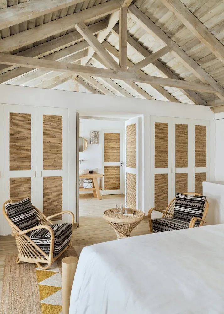 Hell eingerichtetes Schlafzimmer mit Holzgebälk, Flechtsesseln und Schränken mit Strohelementen.