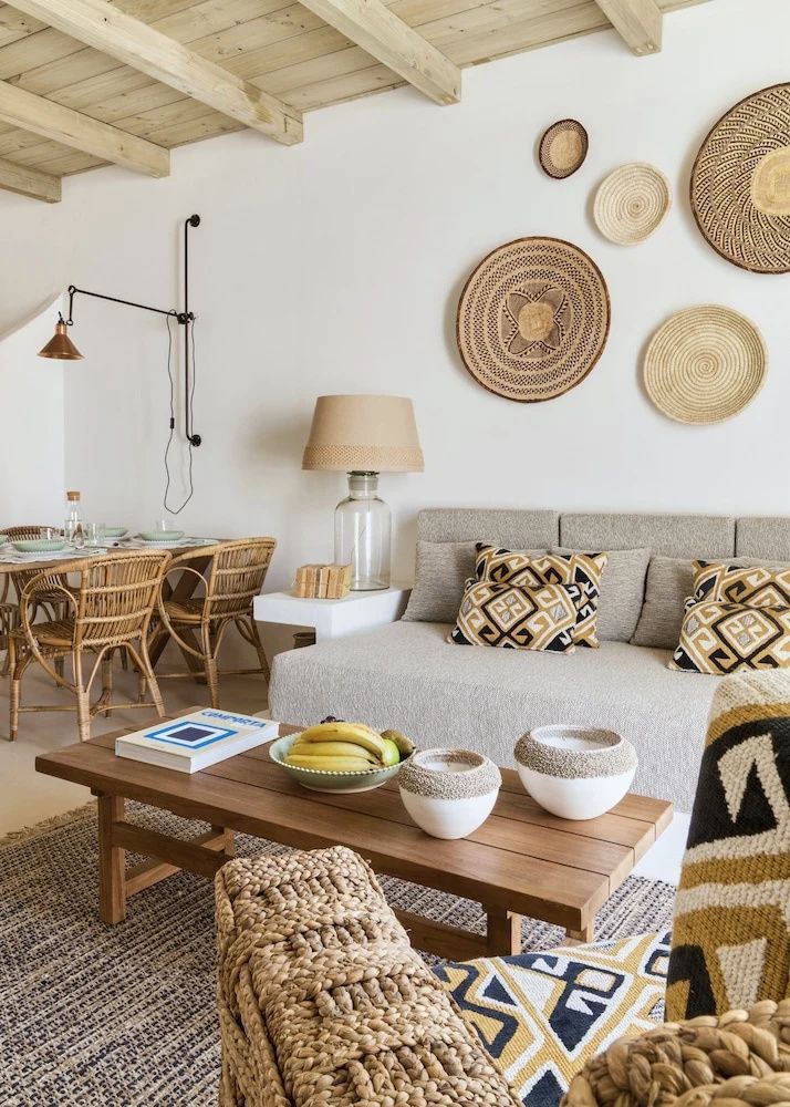 Wohnbereich mit hellem Sofa, Holztisch, Obstschale und Flechtdekoration an der Wand.