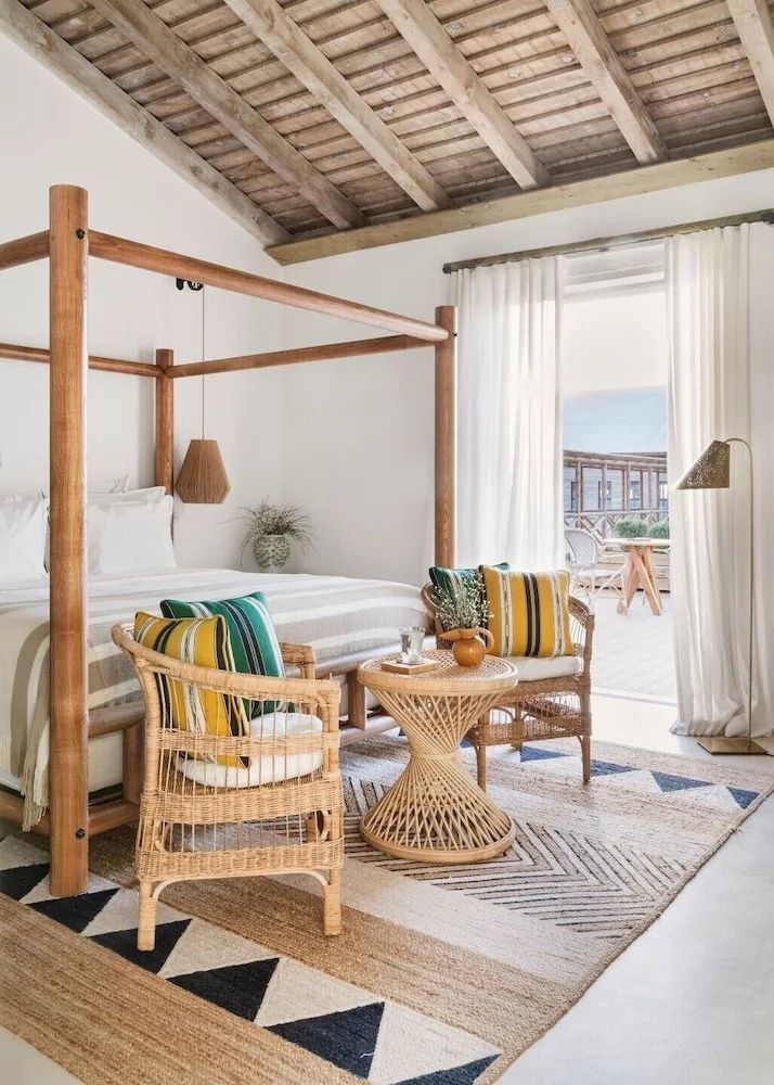 Helles Schlafzimmer mit Holzhimmelbett, Rattanstühlen und Terrassenzugang.