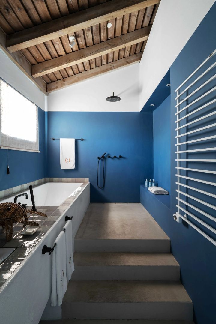 Modernes Badezimmer mit blau gestrichenen Wänden, Badewanne, Regendusche und Decke aus Holz.