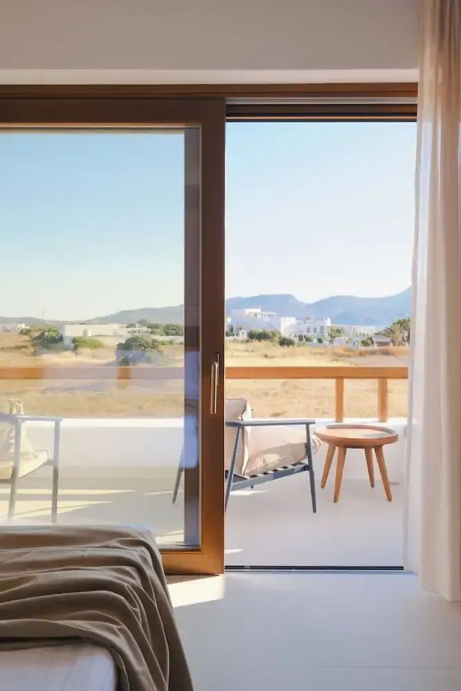 Blick durch die Balkontür auf eine möblierte Terrasse und die hügelige Landschaft.