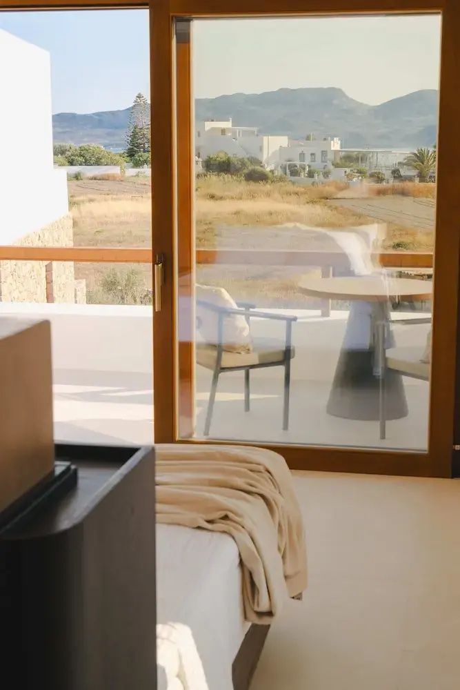 Blick durch die gläserne Balkontür auf den Tisch der Terrasse und die Landschaft dahinter.