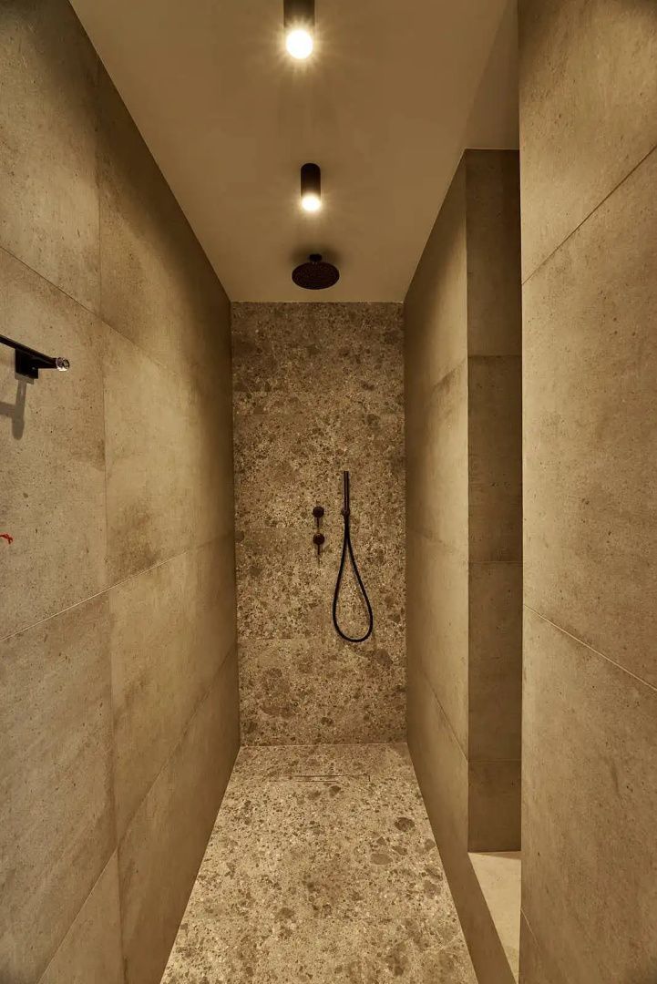 Bodengleiche Dusche mit Steinfliesen und schwarzen Armaturen in einem modernen Badezimmer.