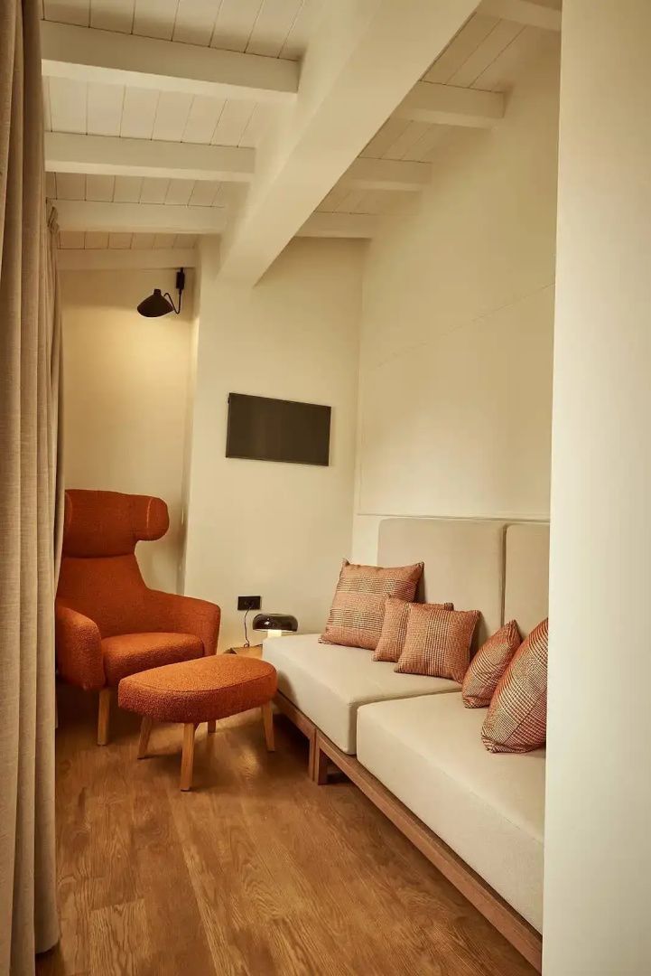Gemütliche Sitzecke im Hotelzimmer mit orangem Sessel, Hocker und einem beigen Sofa
