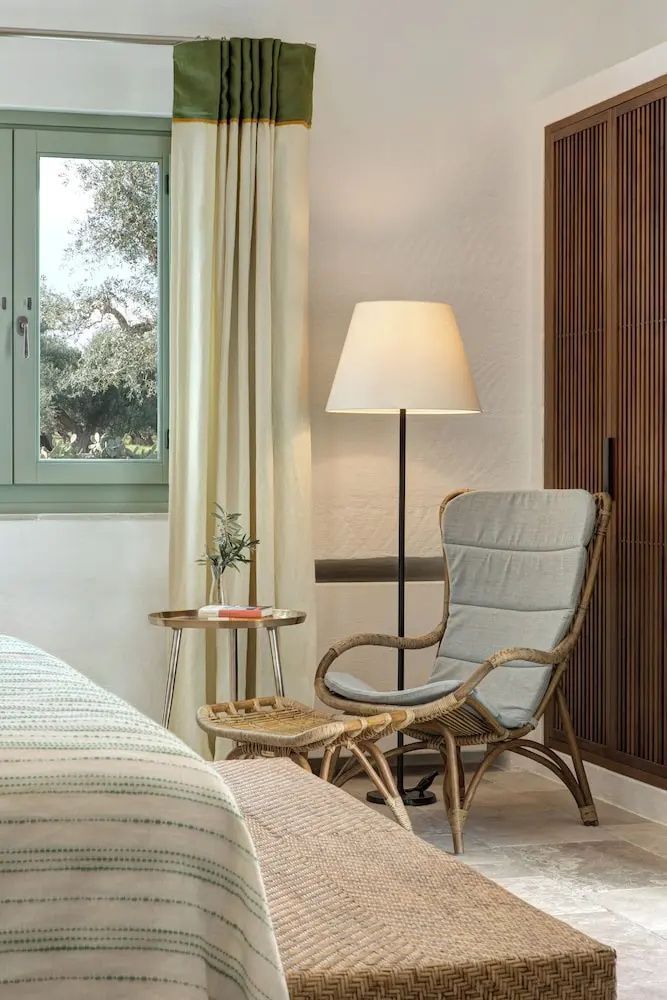 Sitzbereich im Hotelzimmer mit Sessel aus Rattan, Stehlampe und hellen Vorhängen.