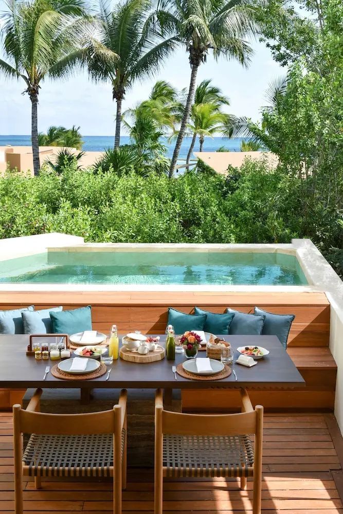 Terrasse mit gedecktem Esstisch, kleinem Pool und Blick auf grüne Palmen und das Meer.