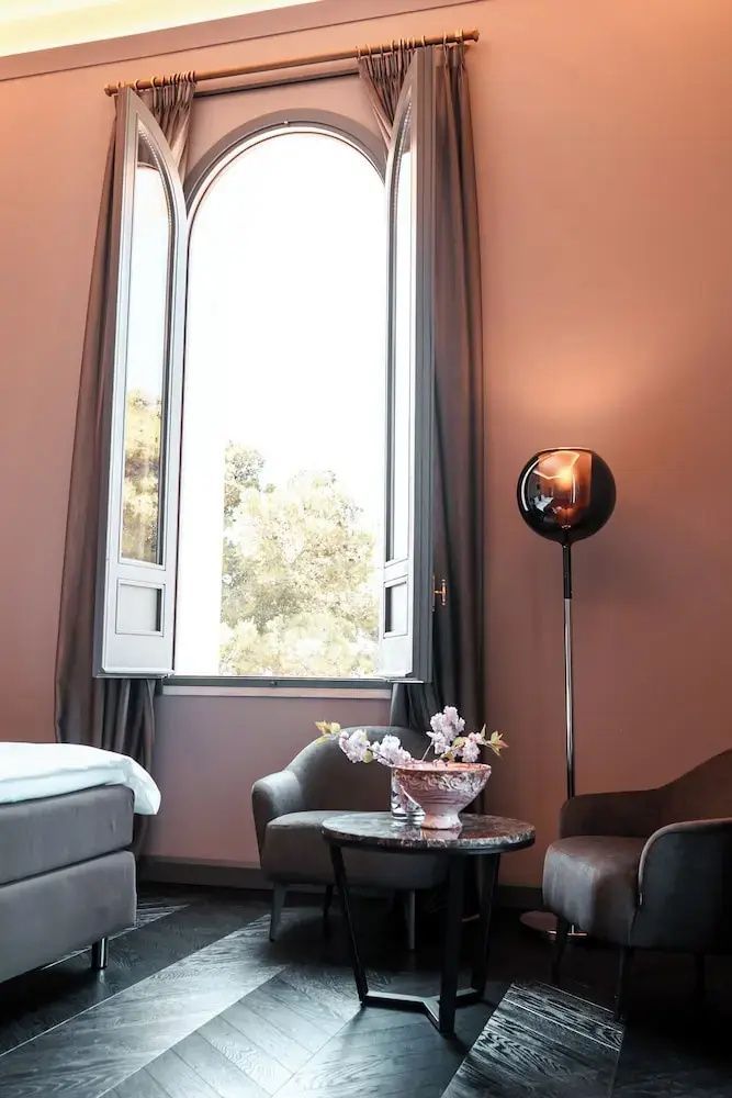 Sitzbereich im Hotelzimmer mit zwei Sesseln, Beistelltisch, Stehlampe und offenem Fenster.
