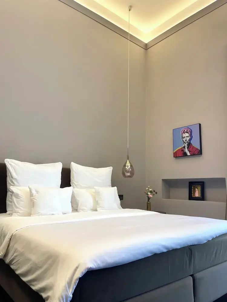 Doppelbett mit mehreren weißen Kissen, tropfenförmiger Hängelampe und kleiner Wandnische.