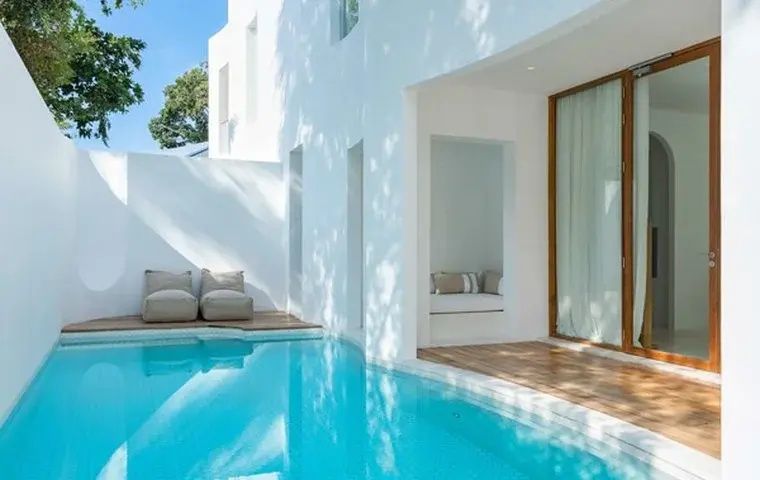 Privater Pool an der weißen Fassade einer Hotelvilla mit Sitzgelegenheiten.