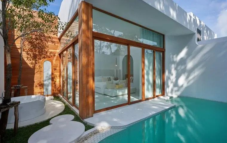 Außenansicht einer Villa mit großen Glasfenstern, Holzrahmen und direkt angrenzendem Pool.