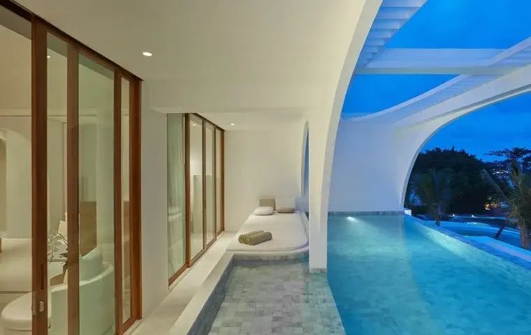 Privater Pool auf der Terrasse mit Liegeplatz unter geschwungenen weisen Bogen am Abend.