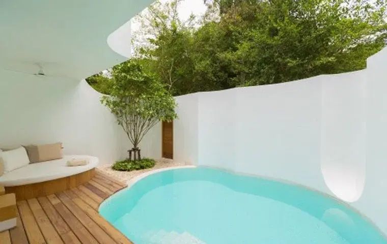 Privater Pool auf einer Holzterrasse, umgeben von weißen Wänden und grünen Pflanzen.